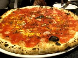 Pizza sabroso pepperoni picante cubierto rebanadas ingredientes de cocina tomates con prosciutto y especias de tomate rojo en la mesa. foto