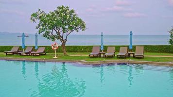 Piscina de sillas alrededor de la piscina con fondo de mar al atardecer - vacaciones y concepto de vacaciones