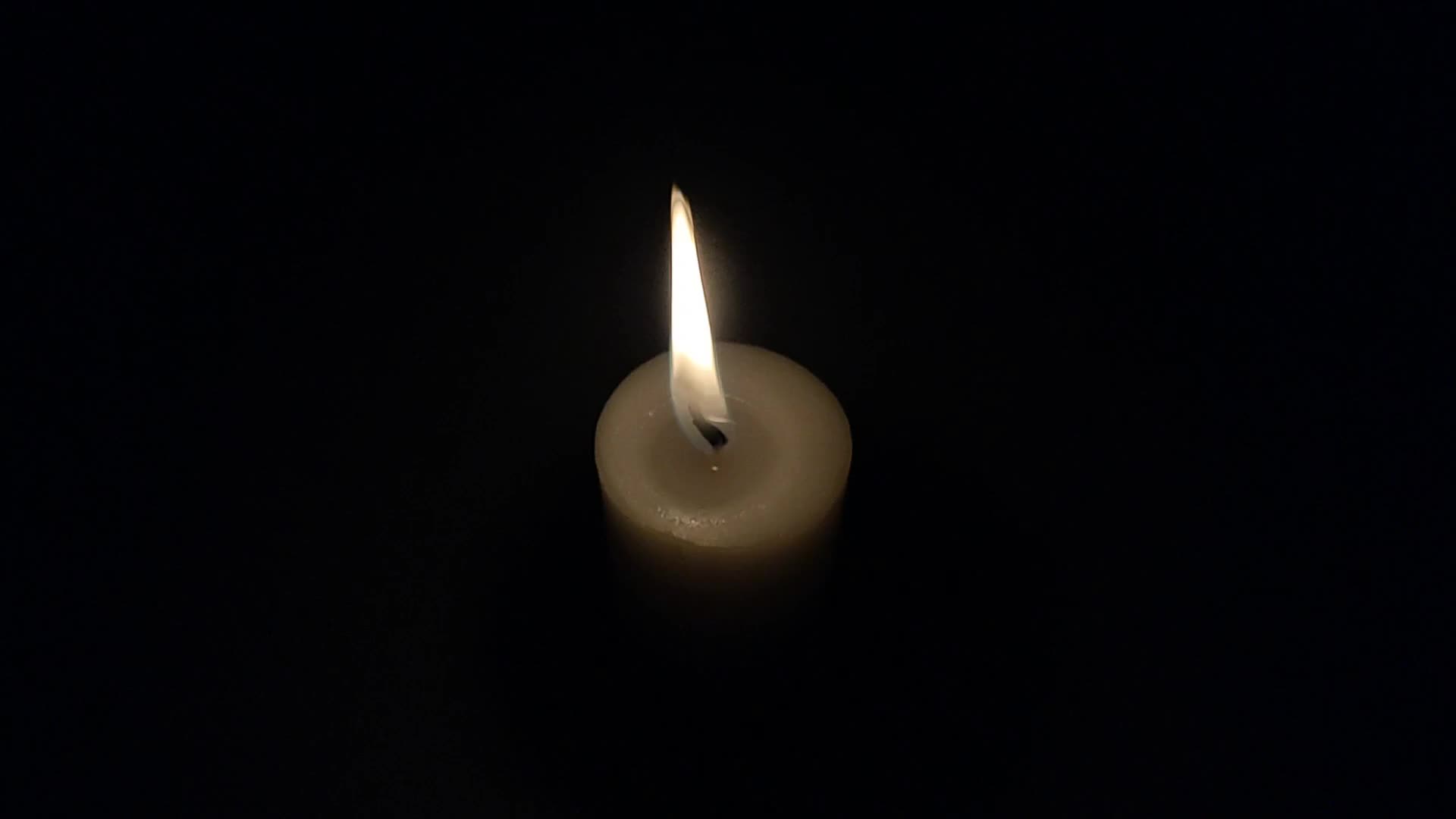 Burning candle on a black background. The candle flame flickers slowly