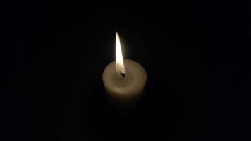 brennende Kerze auf schwarzem Hintergrund. die Kerzenflamme flackert langsam. isoliertes Feuer auf dunklem Hintergrundweiße Kerze, gelbe Flamme in der Nacht. video