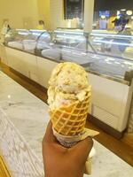 ice cream flavor white chocolate frozen dessert pattern in waffle cone hand holding on table. photo