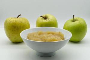 Apple sauce in a white bowl with raw apples on background. Apple puree and fresh green apples isolated on white background. photo