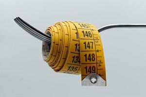 cinta métrica amarilla envuelta alrededor de un tenedor plateado. concepto de dieta y pérdida de peso. foto