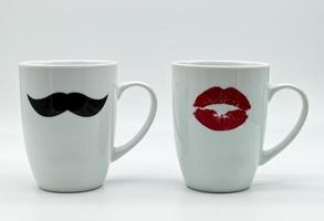 Couple of white ceramic mugs decorated with black male mustache and red female lips, isolated on white background. Romantic Valentines day and marriage concept.