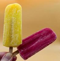 Hand holding yellow and purple Popsicle on a yellow background photo