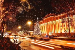 Coches en el tráfico en las horas pico por la noche en la avenida Rustaveli en la ciudad capital de Tbilisi en Georgia en Navidad con árbol de Navidad por el parlamento en el fondo foto