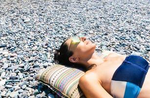 Joven mujer caucásica cabeza recostada sobre una almohada con playa rocosa beackground foto