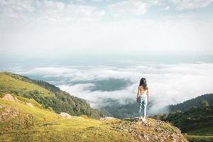 Solo brunette woman relaxed stands on the edge above clouds carefree lifestyle. Adventure and fullflment in life concept. photo