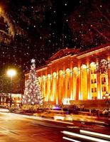 Coches en la carretera en el tráfico en horas punta por la noche en la avenida Rustaveli en la ciudad capital de Tbilisi en Georgia en Navidad con el árbol de Navidad por el parlamento en el fondo foto