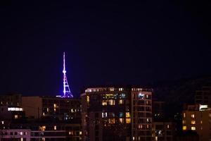 Tbilisi TV communication tower illuminated at night. View Georgia capital and house buildings at night concept background. photo