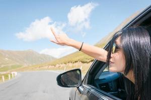 Female caucasian woman from car window points finger up to left with asphalt road background. Copypaste raod trip concept. photo