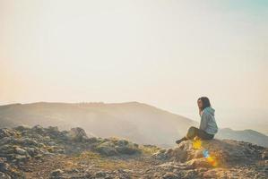 Rear view image of a woman sitting alone on peak mountain looking left blank space bright background photo