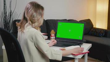 zakenvrouw op laptop met groen scherm maakt aantekeningen van laptop.