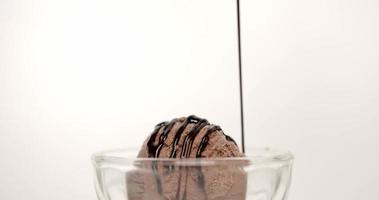 vista frontal, vierte la salsa de chocolate encima del helado. cubitos de helado en una taza de vidrio transparente. sobre el fondo blanco.