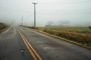 Long lonely paved road passing through a countryside landscape with fields and farms, in a foggy day near Bento Goncalves. A friendly country town in southern Brazil famous for its wine production. photo