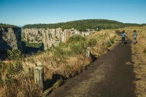Dirt pathway and people at the Itaimbezinho Canyon with steep rocky cliffs in a flat plateau near Cambara do Sul. A small country town in southern Brazil with amazing natural tourist attractions. photo