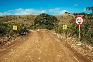 camino de tierra desierto que pasa por tierras bajas rurales llamadas pampas con colinas y señales de tráfico cerca de cambara do sul. una pequeña ciudad rural en el sur de Brasil con increíbles atractivos turísticos naturales. foto