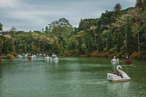 People having fun on fiberglass boats with the shape of swan, in a cloudy day at the Black Lake in Gramado. A cute european-influenced town in southern Brazil, highly sought after by tourists. photo