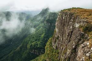 Fortaleza Canyon with steep rocky cliffs covered by thick forest and fog coming up the ravine near Cambara do Sul. A small country town in southern Brazil with amazing natural tourist attractions. photo