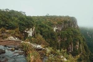 Creek on waterfall edge with steep rocky cliffs covered by forest at Serra Geral National Park near Cambara do Sul. A small country town in southern Brazil with amazing natural tourist attractions. photo