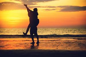 Amantes asiáticos felices en la playa con una hermosa puesta de sol de fondo hombre levantando a la mujer. foto