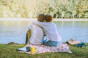 Asian couple lover sitting a relax River side in the public park. working with a notebook and drinking coffee.in the park. in the holiday. photo