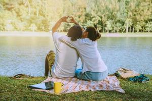 Asian couple lover sitting a relax River side in the public park. working with a notebook and drinking coffee.in the park. in the holiday. photo