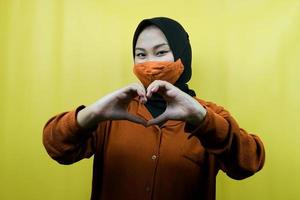 Muslim woman wearing mask, with hands sign of love, affection, happy, isolated photo