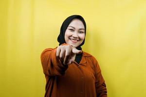 Beautiful young asian muslim woman with hands pointing at camera, wanting you, pointing at you, wanting to be with you, smiling confident, enthusiastic and cheerful, facing the camera, isolated