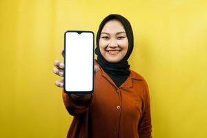 Beautiful young asian muslim woman holding smartphone with white or blank screen, promoting app, promoting something, isolated, advertising concept photo