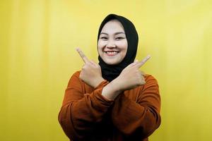 Beautiful young asian muslim woman with hands pointing empty space presenting something, looking at camera isolated, advertising concept photo