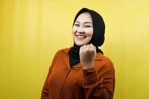Beautiful young asian muslim woman with hands clenched, sign of success, punching, fighting, not afraid, victory, smiling confident, enthusiastic and cheerful, isolated photo