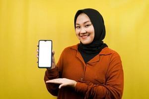 Beautiful young asian muslim woman holding smartphone with white or blank screen, promoting app, promoting something, isolated, advertising concept photo