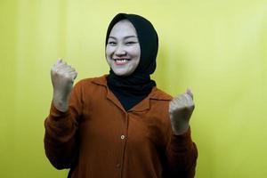 Beautiful young asian muslim woman with hands clenched, sign of success, punching, fighting, not afraid, smiling confident, enthusiastic and cheerful, isolated photo