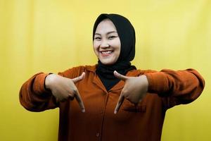 Beautiful asian young muslim woman with hands pointing down, hands click the link below, hands presenting something, isolated photo