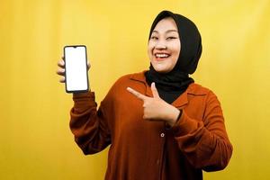 Beautiful young asian muslim woman shocked, surprised, wow expression, hand holding smartphone with white or blank screen, promoting app, promoting product, presenting something, isolated photo