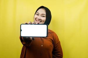 Beautiful young asian muslim woman holding smartphone with white or blank screen, promoting app, promoting something, isolated, advertising concept photo