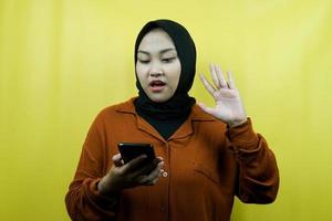Beautiful young asian muslim woman shocked, surprised, with hands holding smartphone, looking at smartphone, looking at promo, isolated, advertising concept photo