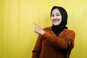 Beautiful young asian muslim woman with hands pointing empty space presenting something, smiling confident, enthusiastic, cheerful, looking at camera, isolated, advertising concept photo