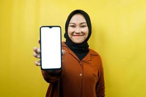 Hermosa joven musulmana asiática sosteniendo un teléfono inteligente con pantalla blanca o en blanco, promocionando la aplicación, promocionando algo, aislado, concepto publicitario foto