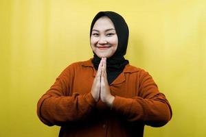 Beautiful asian young muslim woman with hands on face, apologizing, smiling confident, enthusiastic and cheerful, facing camera isolated photo