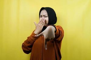 Beautiful young muslim woman with hand covering mouth, hand pointing down, showing disapproval expression, showing disgust at something, isolated photo