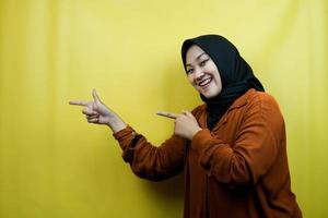 Beautiful young asian muslim woman with hands pointing at empty space, presenting something, isolated photo