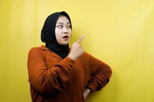 Beautiful young asian muslim woman shocked, surprised, wow expression, with hand pointing to empty space, presenting something, presenting product, isolated photo