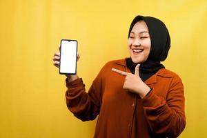 Beautiful young asian muslim woman shocked, surprised, wow expression, hand holding smartphone with white or blank screen, promoting app, promoting product, presenting something, isolated photo