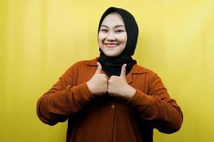 Beautiful young asian muslim woman with hands thumbs up, ok sign, good job, success, victory, smiling confident, enthusiastic and cheerful, looking at camera isolated photo