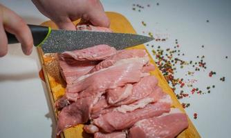 Sliced pieces of meat with a knife on a kitchen board and pepper photo