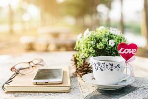 Close-up of empty notebook,smartphone,spectacles and cup of coffee on Marble floor background. Love concept with heart desktop,Valentine's Day. photo