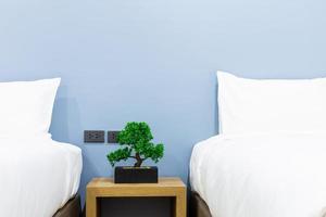 Close-up of white pillow on bed decoration with light lamp and green tree in flowerpots in hotel bedroom interior. photo