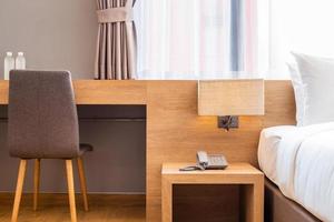 Close-up of white pillow on bed decoration with light lamp, chair and digital telephone set in hotel bedroom interior. photo